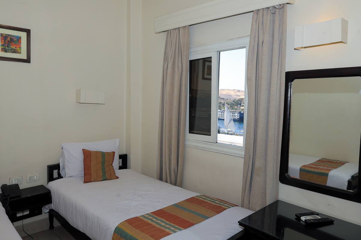 A hotel room with a bed, a nightstand, a mirror, and a window with curtains.