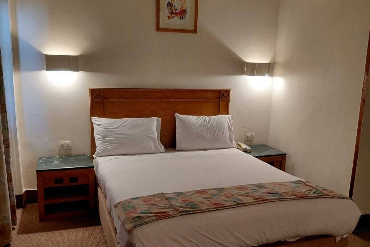 A hotel room with a bed, bedside tables, a chair, and a framed picture on the wall.