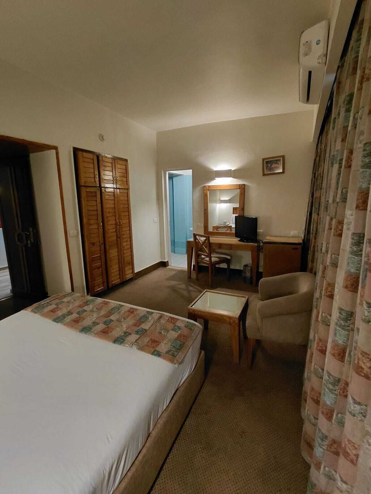 Habitación de hotel con cama, escritorio, silla, televisor y armario.