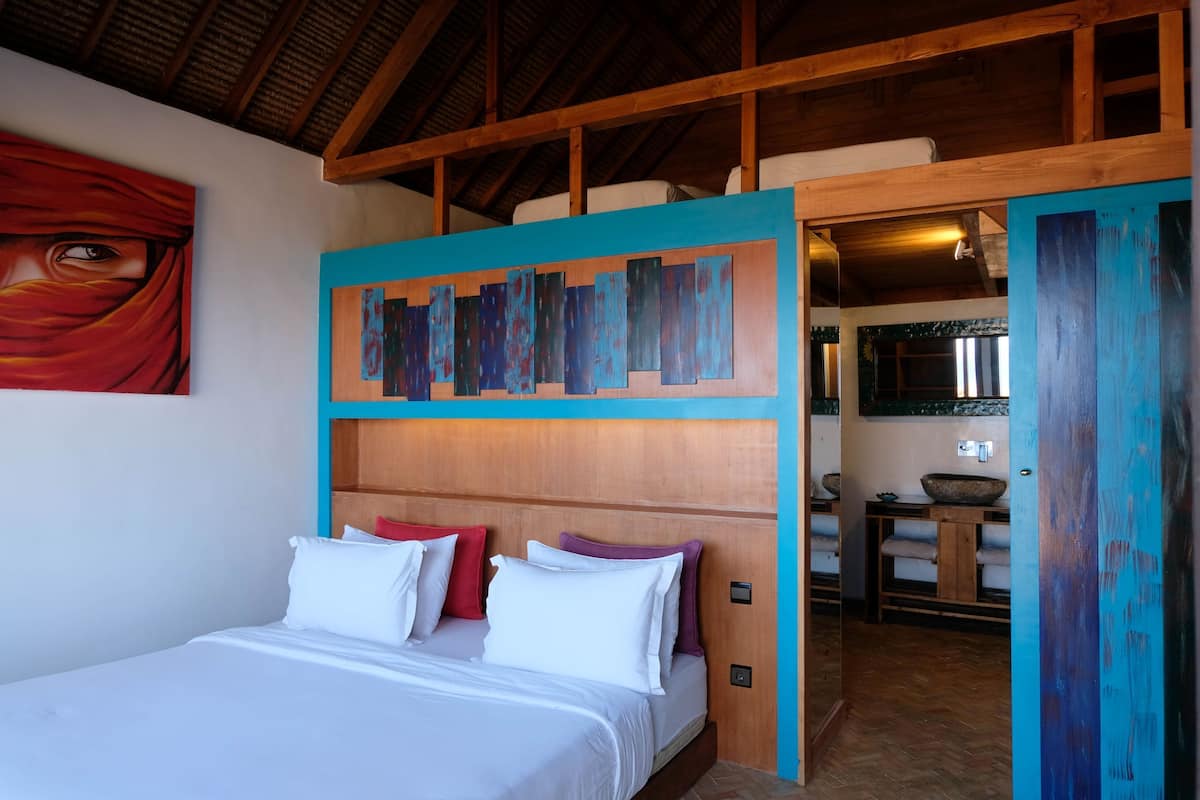 Une chambre à coucher avec une tête de lit en bois, un lit avec des oreillers blancs et rouges, et un tableau accroché au mur.