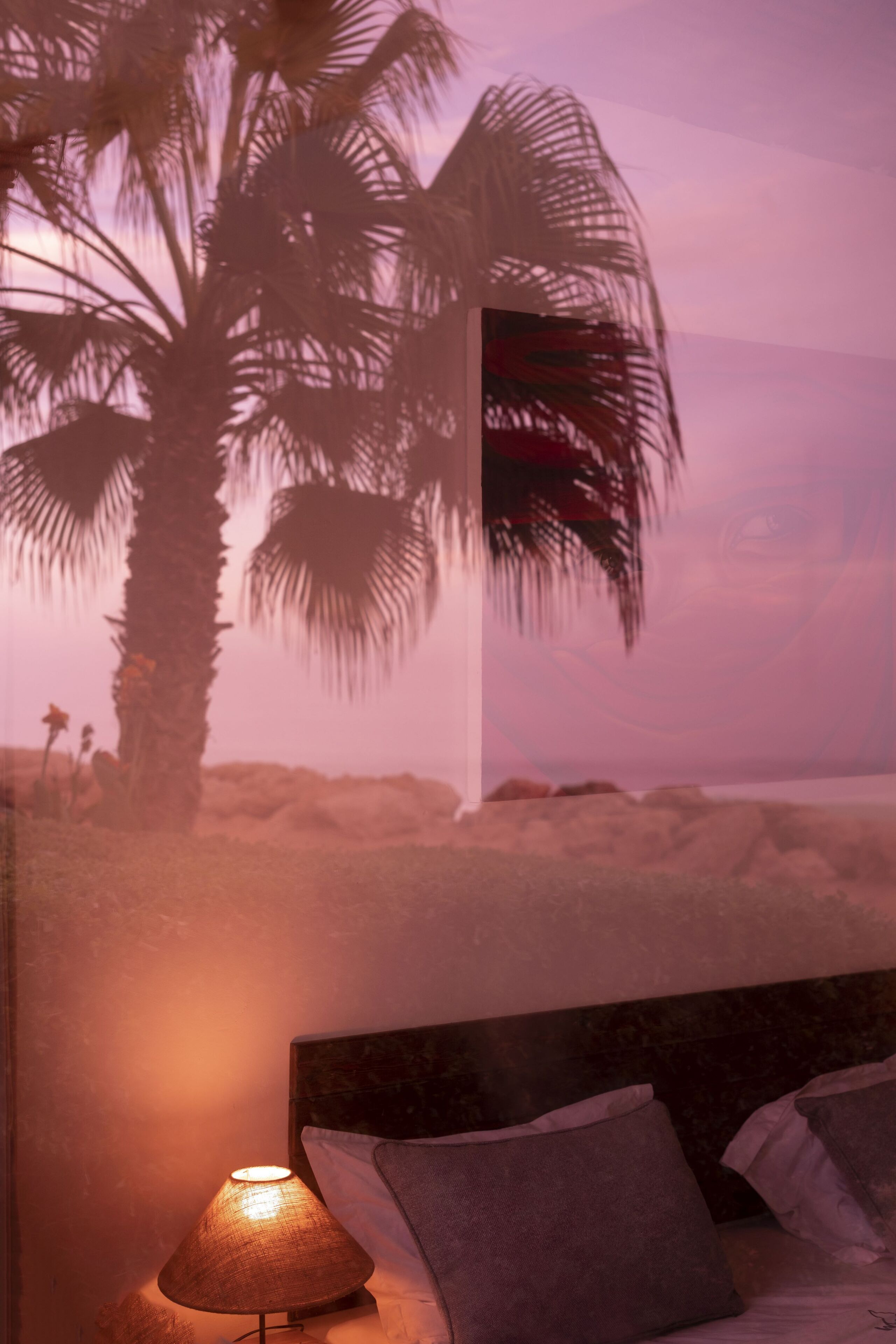 A bedroom with a bed, pillows, a nightstand, a lamp, and a wall mural of a beach scene.