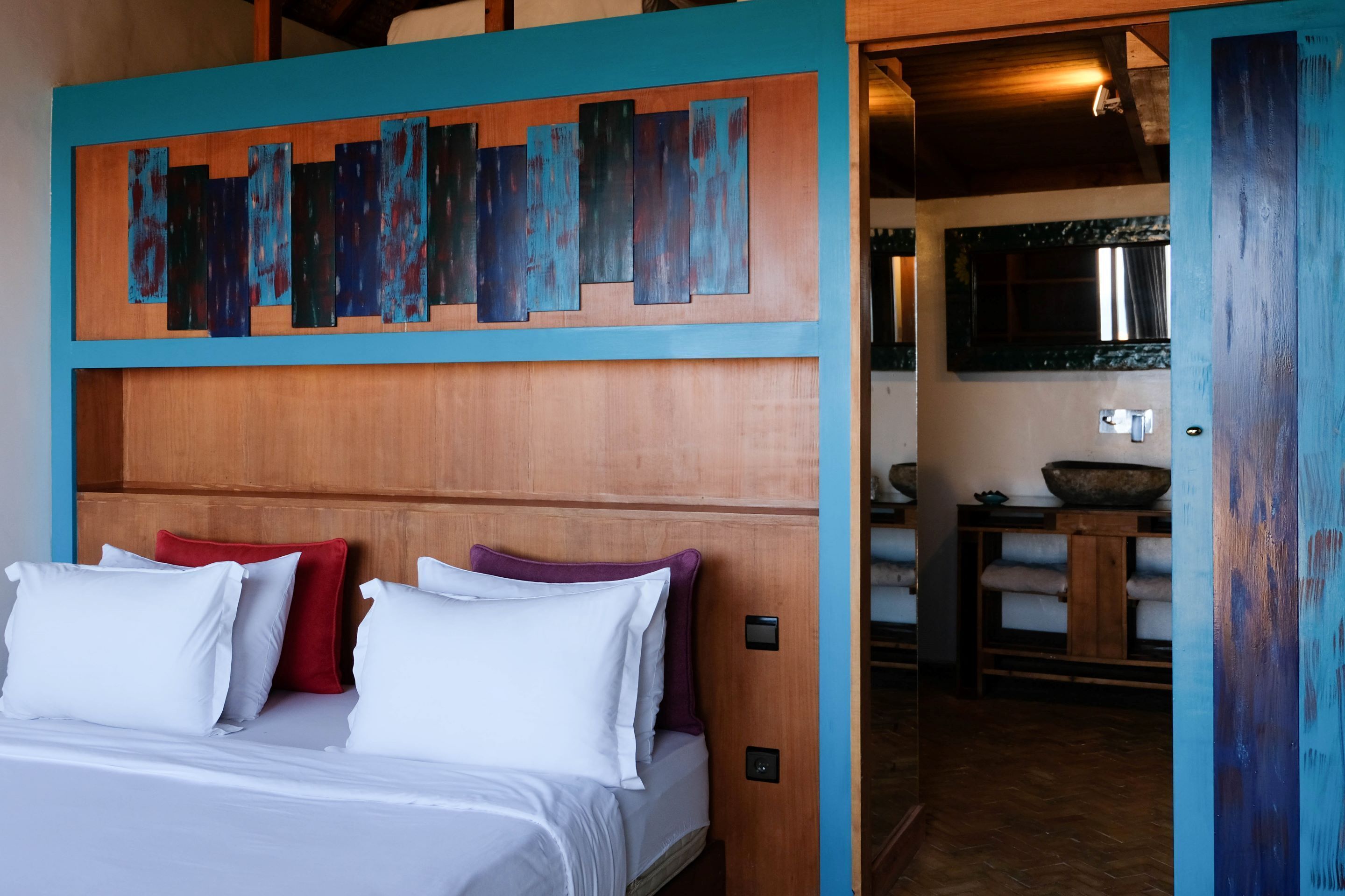 A bedroom with a wooden headboard, a bed with white and red pillows, and a blue accent wall.