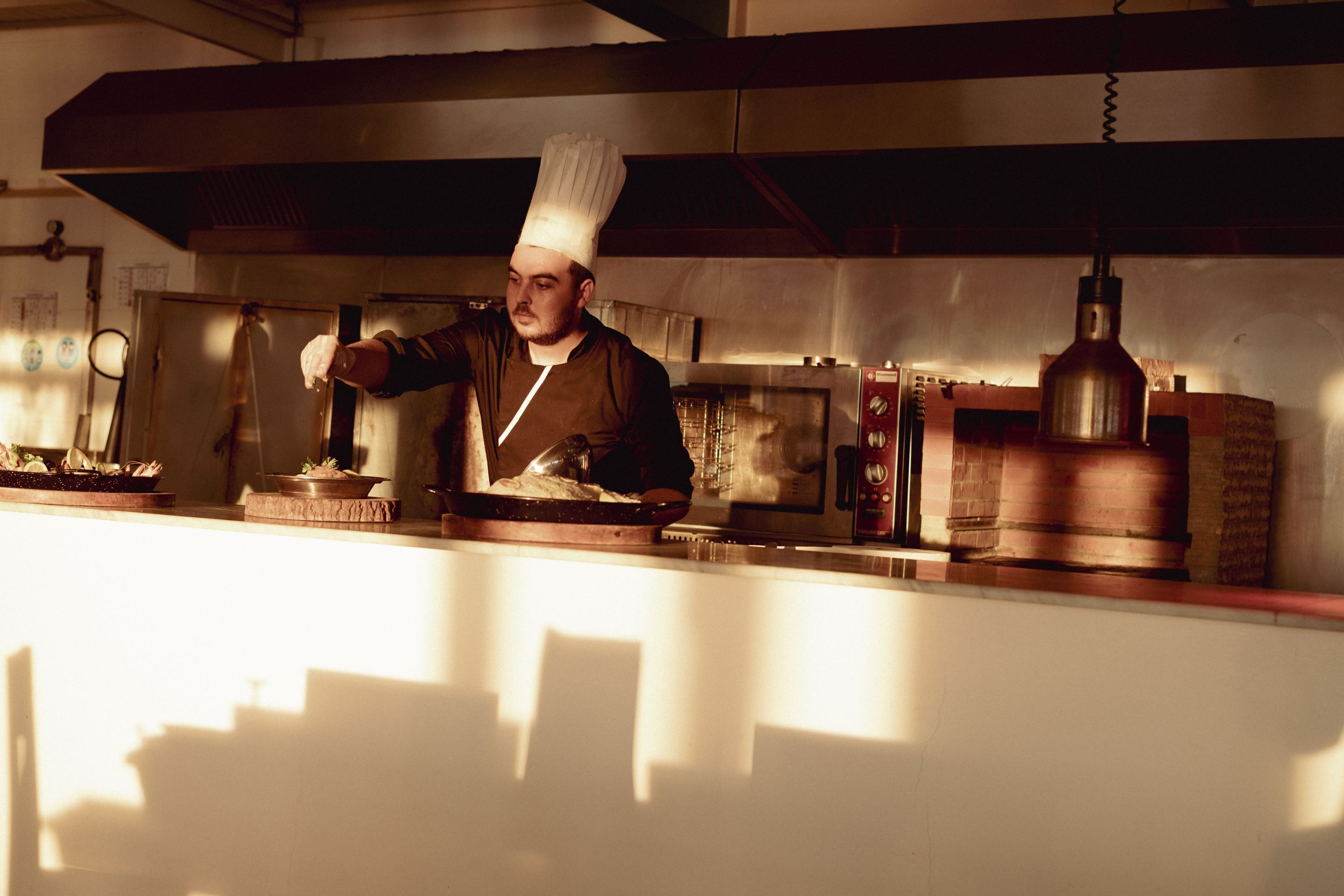 A chef in a professional kitchen with stainless steel appliances and a brick oven.