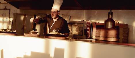 A chef in a professional kitchen with stainless steel appliances and a brick oven.