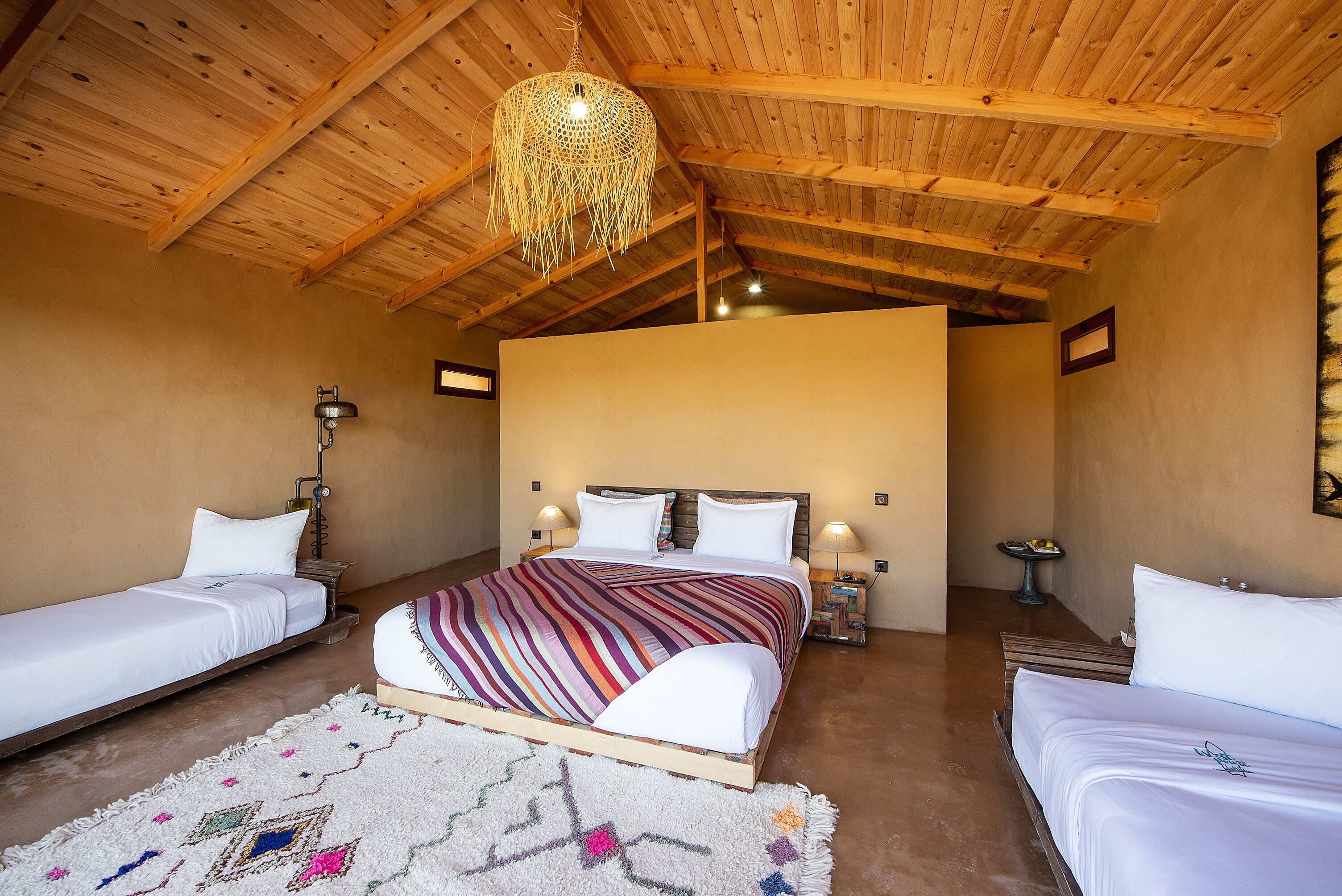A bedroom with a large bed, two smaller beds, wooden ceiling beams, and a hanging light fixture.