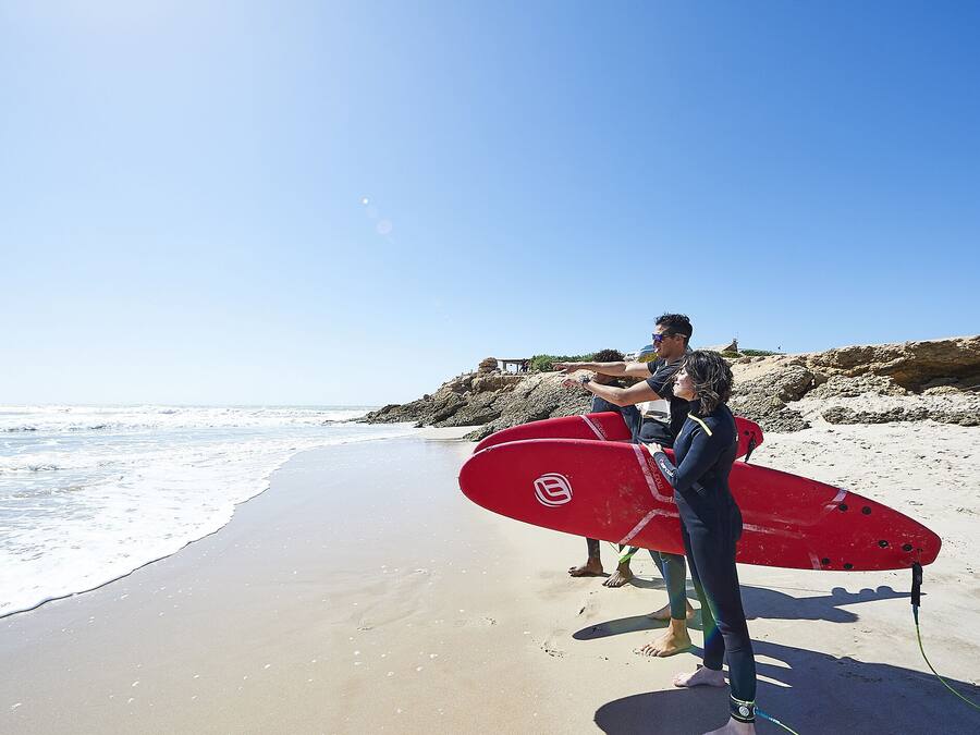 Ein Strand mit blauem Himmel, einem roten Surfbrett und felsigem Gelände.