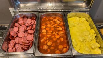 Buffetissa on kolme tarjotinta, joilla on tarjolla seuraavaa: viipaloitua makkaraa, porkkanoita sisältävää pataruokaa sekä makaronia ja juustoa.