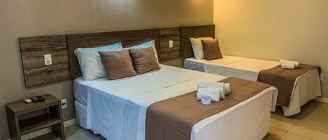 A hotel room with two beds, a nightstand, and wall-mounted lighting.
