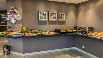 A hotel buffet with a variety of food options, framed pictures on the wall, and a trash bin.