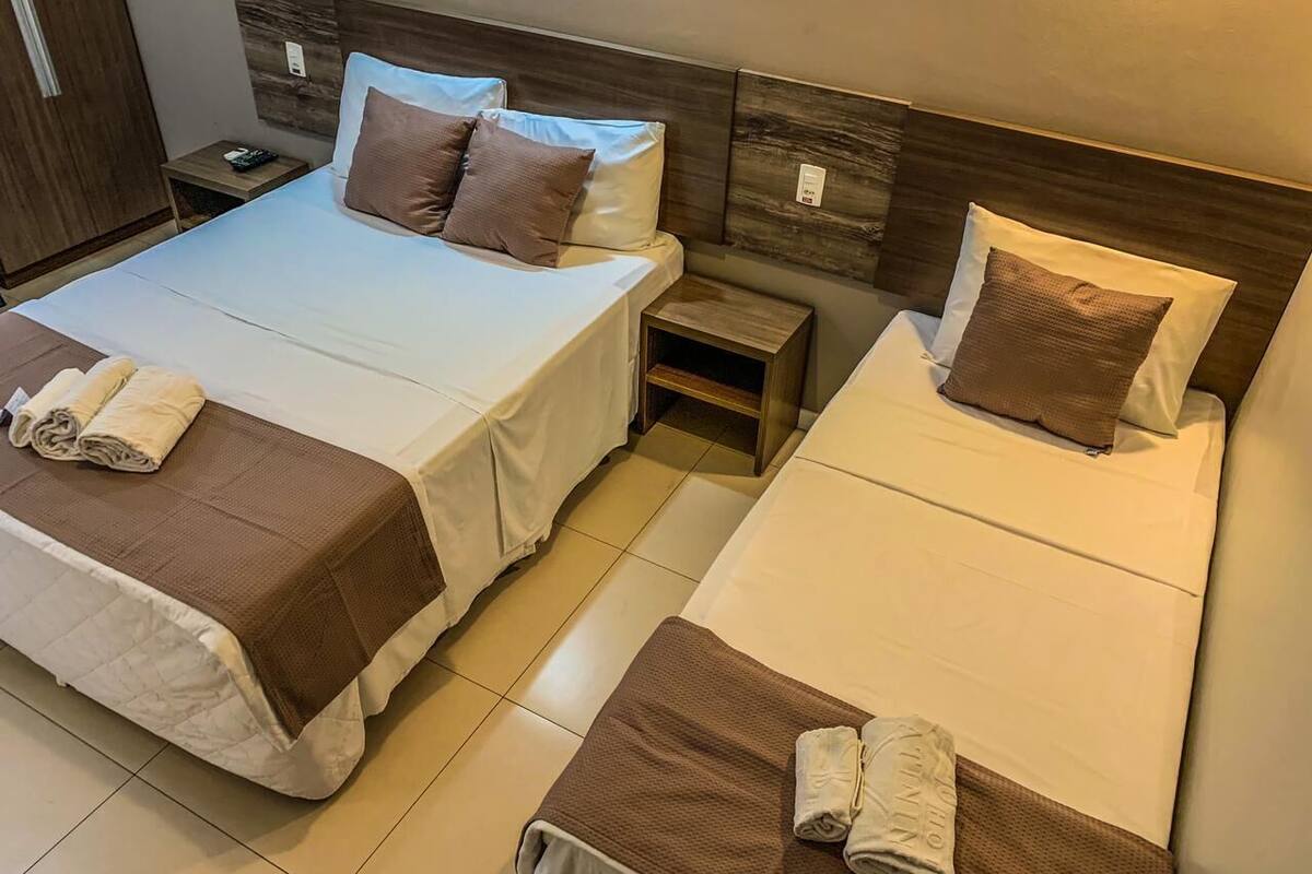 A hotel room with two beds, each with a brown bedspread and pillows, a nightstand with a phone, and a small wooden shelf.