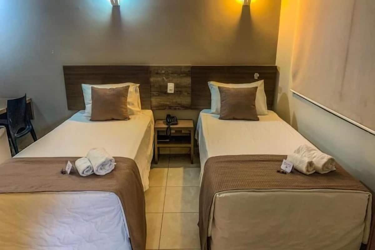 A hotel room with two beds, each with a headboard, bedside tables, and lamps.