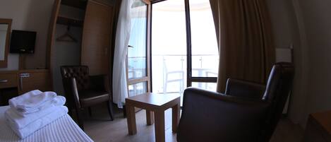 Une chambre d’hôtel comprenant un lit, un bureau, une chaise, une petite table et un balcon avec des rideaux.