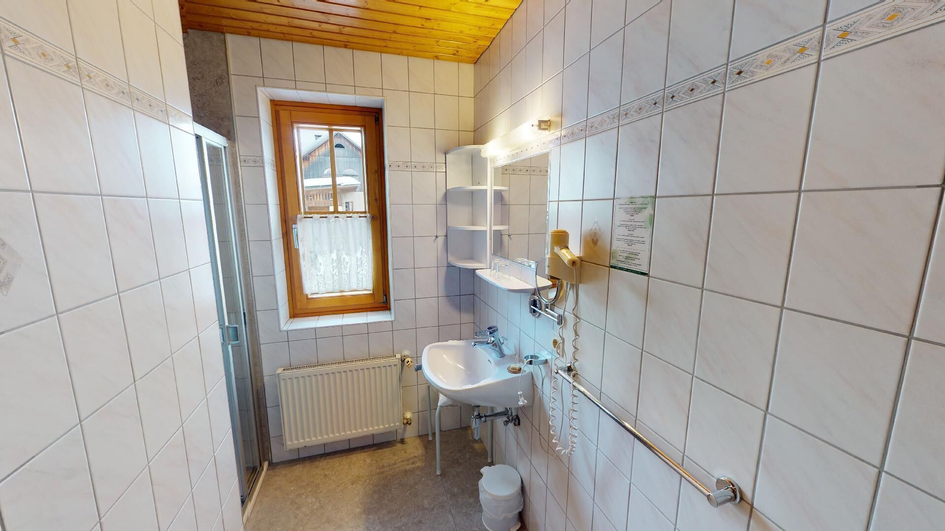 A small bathroom with white tiles, a window with a wooden frame, a radiator, a sink, and a towel rack.