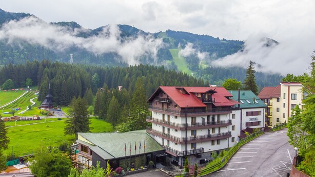 A multi-story hotel with a red roof, surrounded by lush greenery and mountains. - Royal Boutique Hotel Poiana Brasov (Brasov)