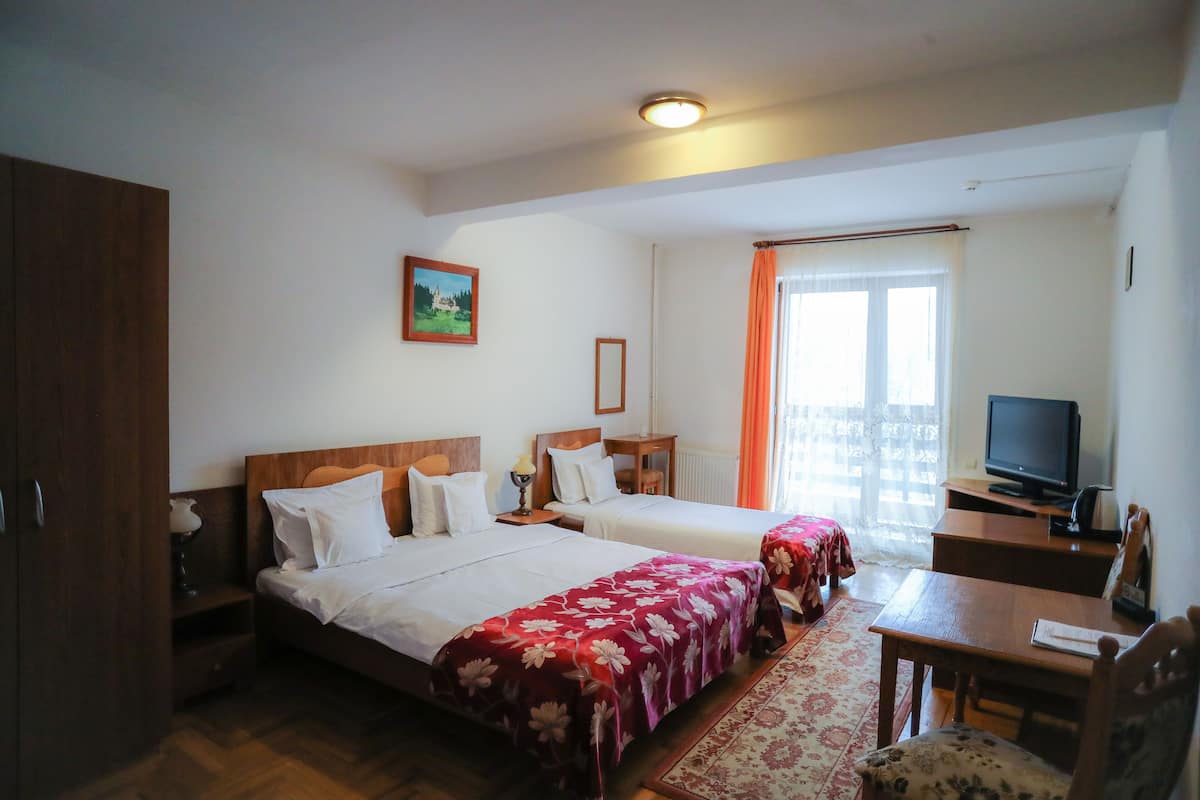 A hotel room with two beds, a desk, a chair, a television, and a window with curtains.