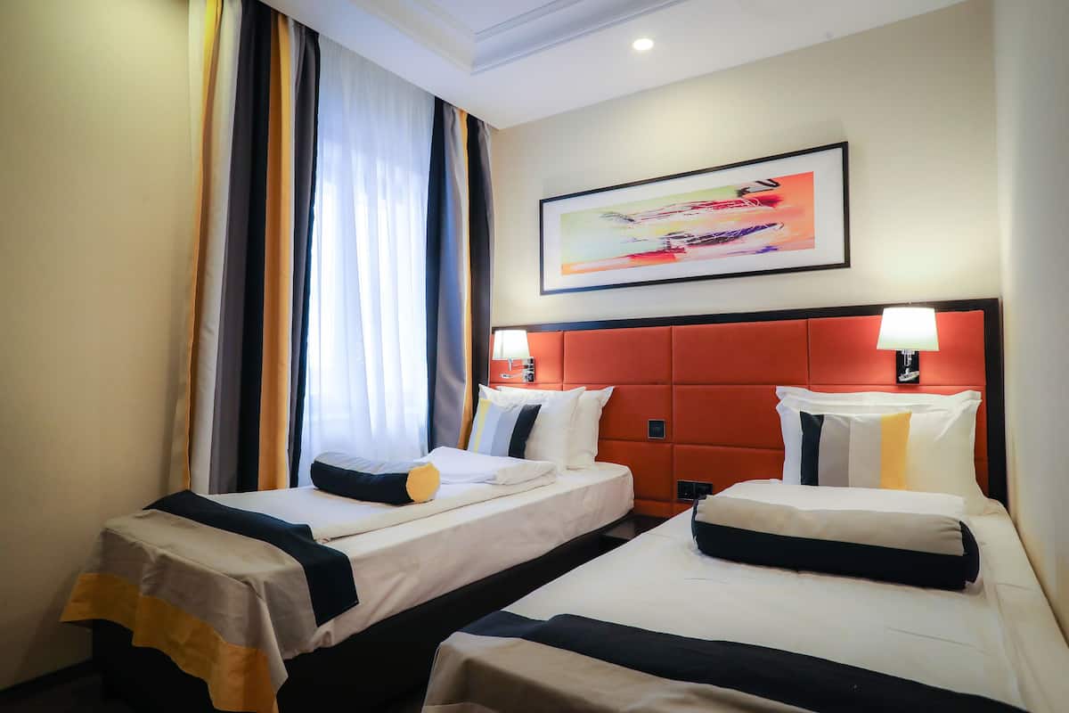 A hotel room with two beds, a red headboard, a painting on the wall, and a window with curtains.