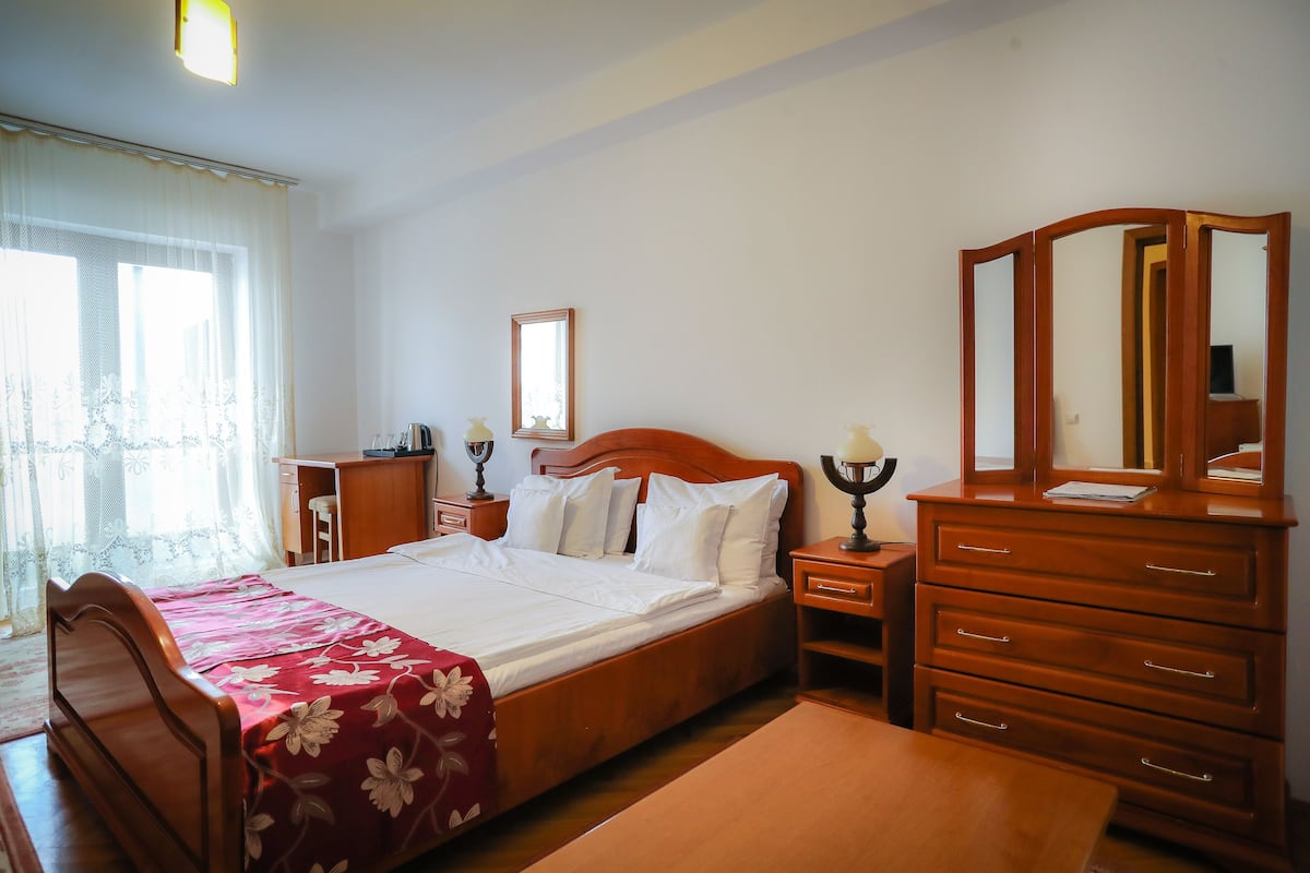 A bedroom with a wooden bed, a dresser with drawers, a nightstand, a desk, and a chair.