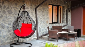 A stone wall, a hanging chair with red cushions, wicker furniture, and a window with vertical blinds. - Royal Boutique Hotel Poiana Brasov (Brasov)