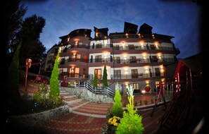A multi-story hotel with balconies, a staircase, and a well-lit entrance.