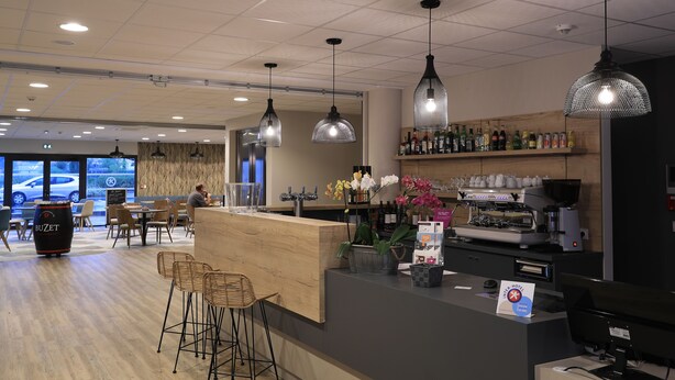 L’intérieur d’un café moderne, avec un comptoir en bois, des tabourets de bar, des lampes suspendues et une machine à café.