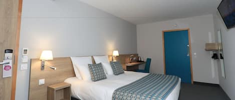 Habitación de hotel con cama, mesitas de noche, escritorio, silla, televisor y puerta.