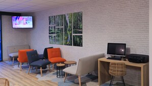 Un espace de détente moderne avec un mur en briques blanches, un grand téléviseur à écran plat et différents types de sièges, notamment des fauteuils orange et gris.