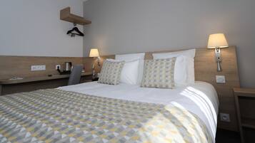 Ein Hotelzimmer mit einem ordentlich bezogenen Bett, Nachttischen mit Lampen, einem Holz-Kopfteil und einem an der Wand befestigten Regal.