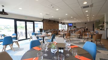 A restaurant with multiple tables, chairs, and a television screen.
