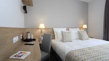 Una habitación de hotel con una cama, dos lámparas de noche, un escritorio con un control remoto, una revista y una cafetera.