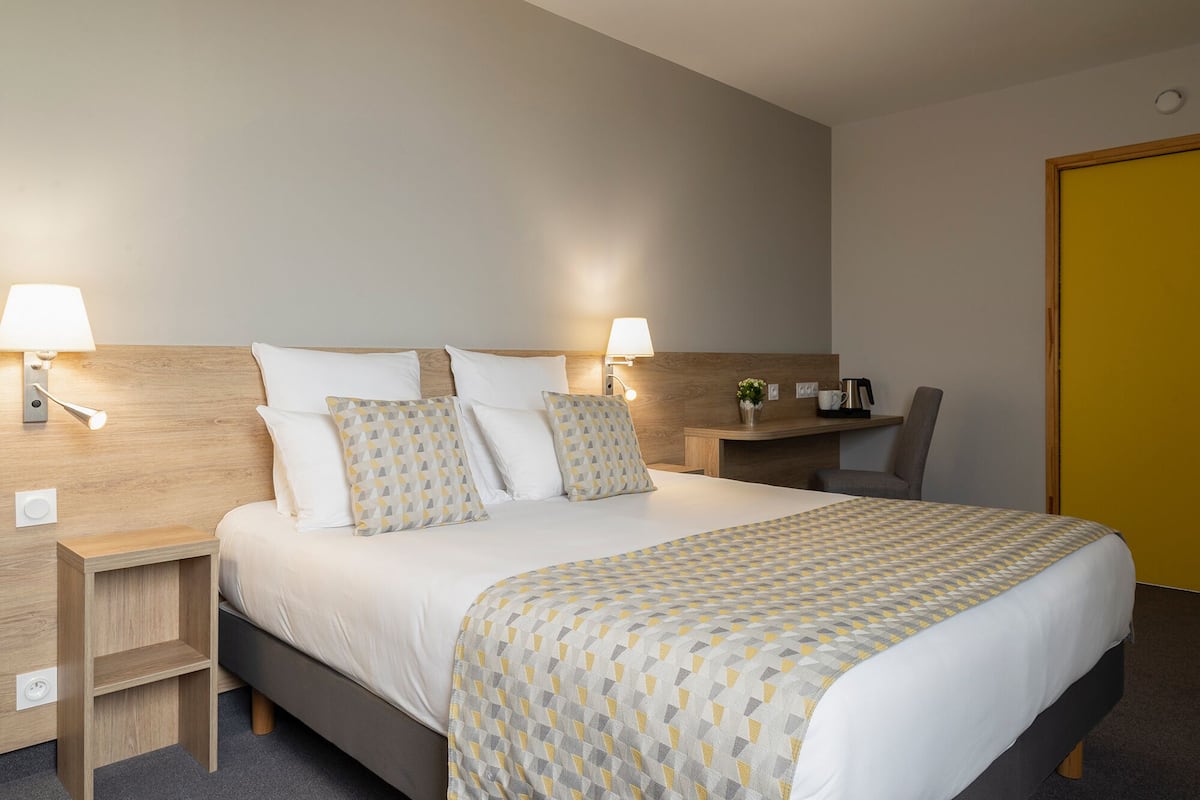 Une chambre d’hôtel avec un lit, deux tables de chevet, un bureau, une chaise et une porte jaune.