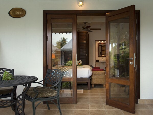 A room with a bed, a small table with chairs, a ceiling fan, and a glass door leading to a balcony.