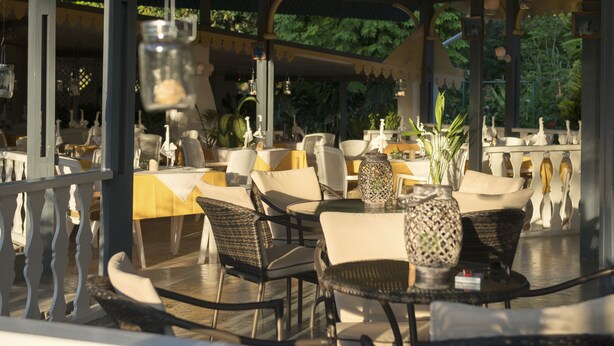 An outdoor café with wicker chairs and tables, surrounded by a white fence and featuring hanging lanterns. - Auberge Chez Plume (Mahé Island)