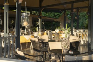 An outdoor café with wicker chairs and tables, surrounded by a white fence and featuring hanging lanterns.