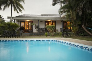 A swimming pool with a tiled edge, surrounded by outdoor furniture and plants. - Auberge Chez Plume (Mahé Island)