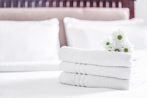 Una cama bien hecha con sábanas blancas y una pila de toallas dobladas.