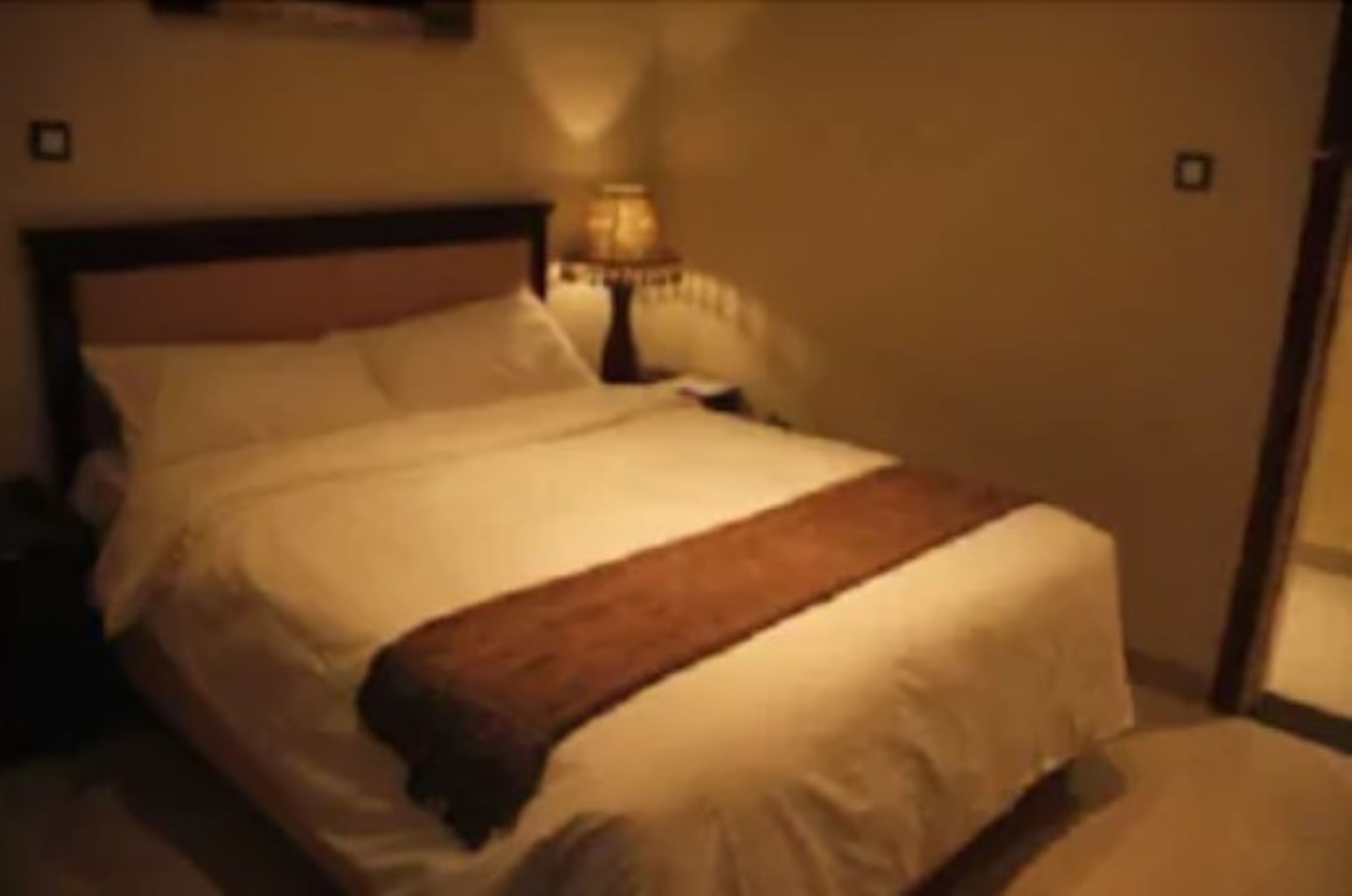 A bed with white linens and a brown throw blanket.