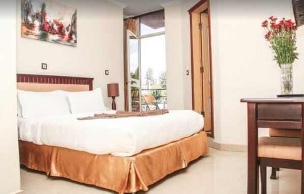A bedroom with a bed, a desk, and a chair. There is a window with a view of the outdoors.