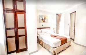 A hotel room with a bed, a wardrobe, and a painting on the wall.