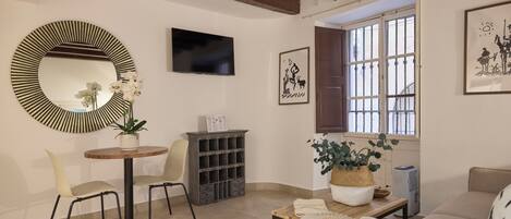 A living room with a round mirror, a television, a bookshelf, a sofa, and a window with a view.