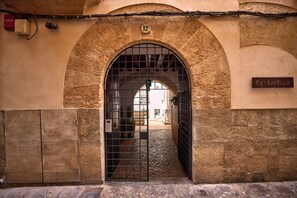 Una entrada arqueada con una reja metálica, un muro de piedra y un cartel que dice "CAN SAVELLA".