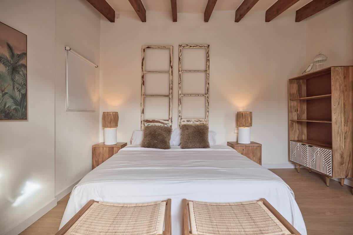 Un dormitorio con una cama grande, cabecera de madera, dos mesitas de noche con lámparas, un armario de madera y un cuadro en la pared.