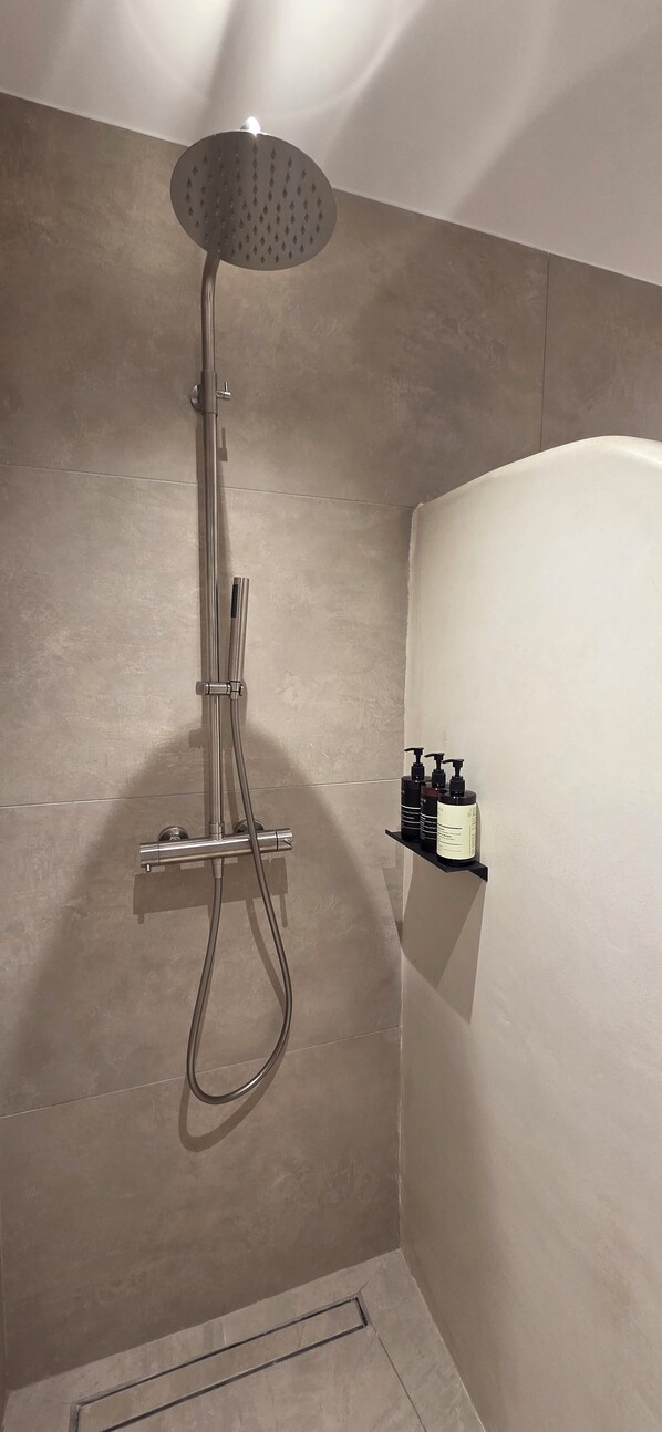 A shower with a handheld showerhead and a wall-mounted control panel.
