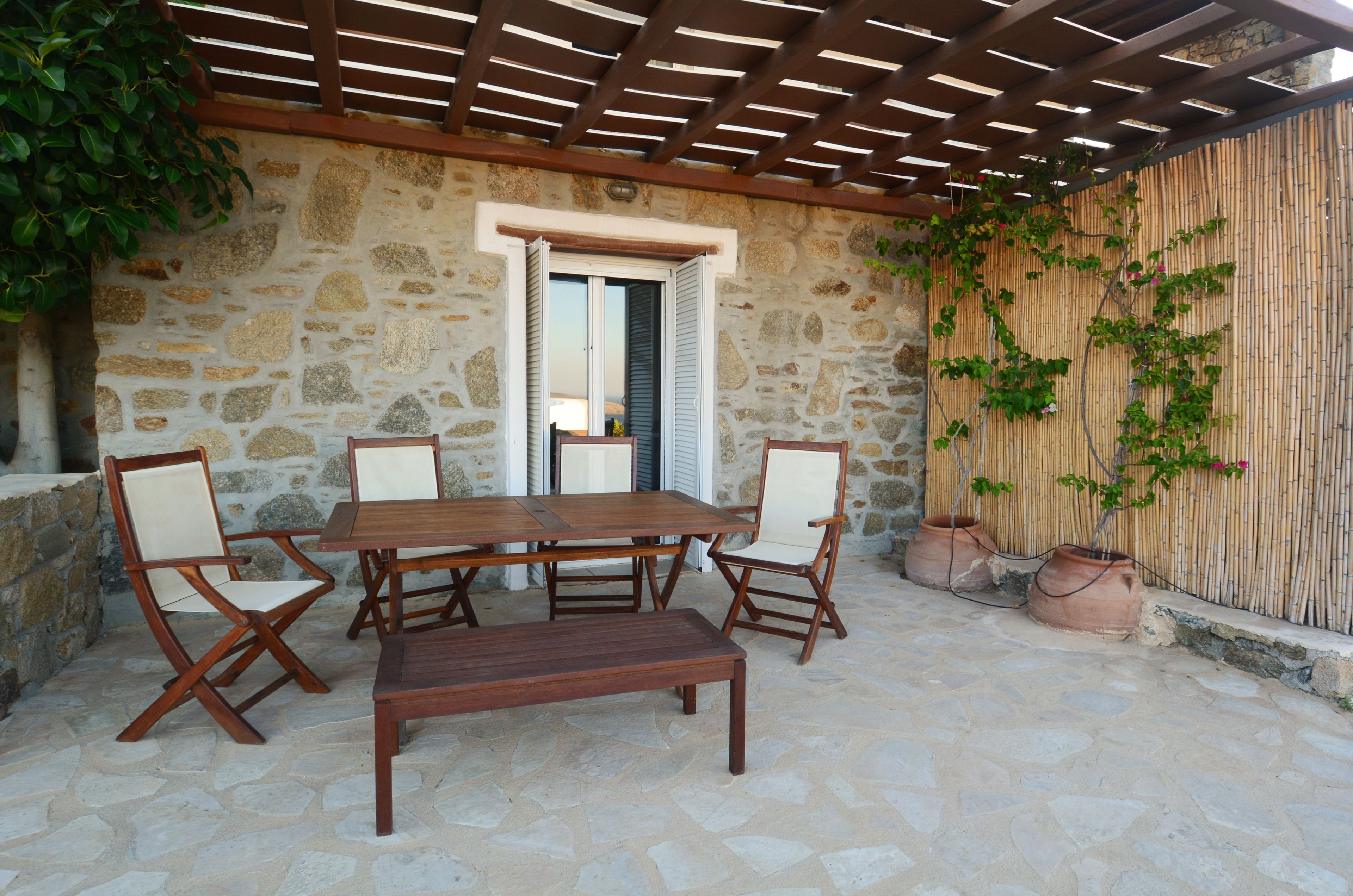 Un patio in pietra con tavolo e sedie di legno, una pergola e un muro in bambù.