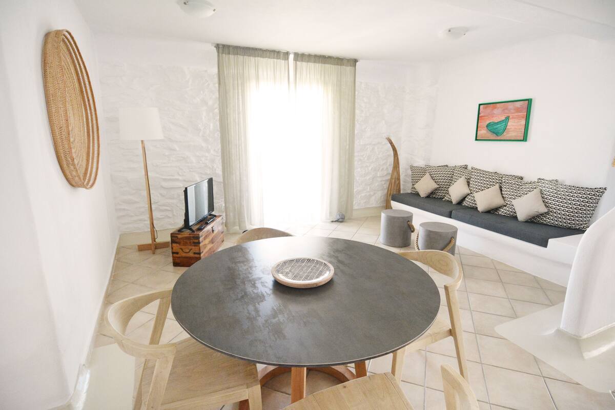 Un comedor con una mesa redonda, sillas, un televisor y un sofá con cojines estampados.