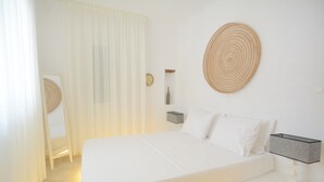 Quarto de hotel bem arrumado com uma cama grande, uma mesa de cabeceira com abajur, um relógio fixado na parede e um objeto decorativo tecido.