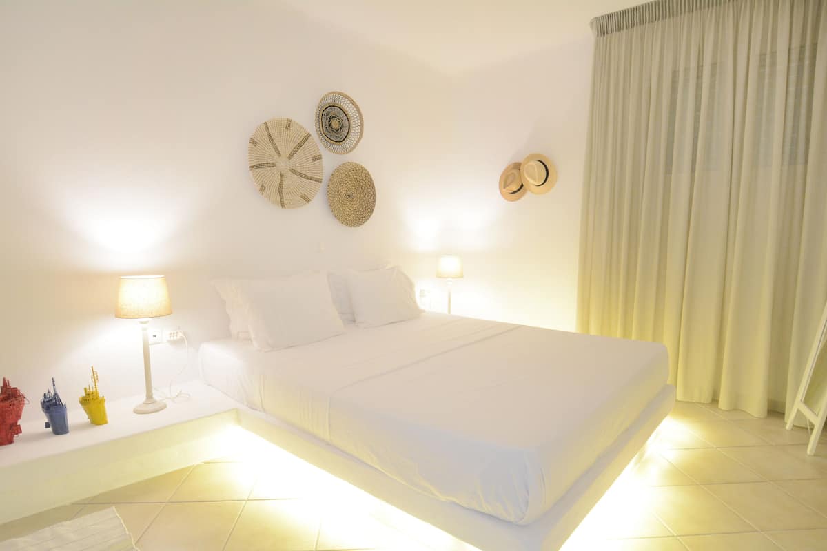 Una cama bien hecha con ropa blanca, dos lámparas de noche y decoración en la pared.