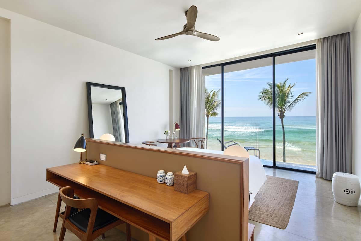Una habitación de hotel moderna con un escritorio de madera, una silla, una mesita, un espejo y vista al océano.