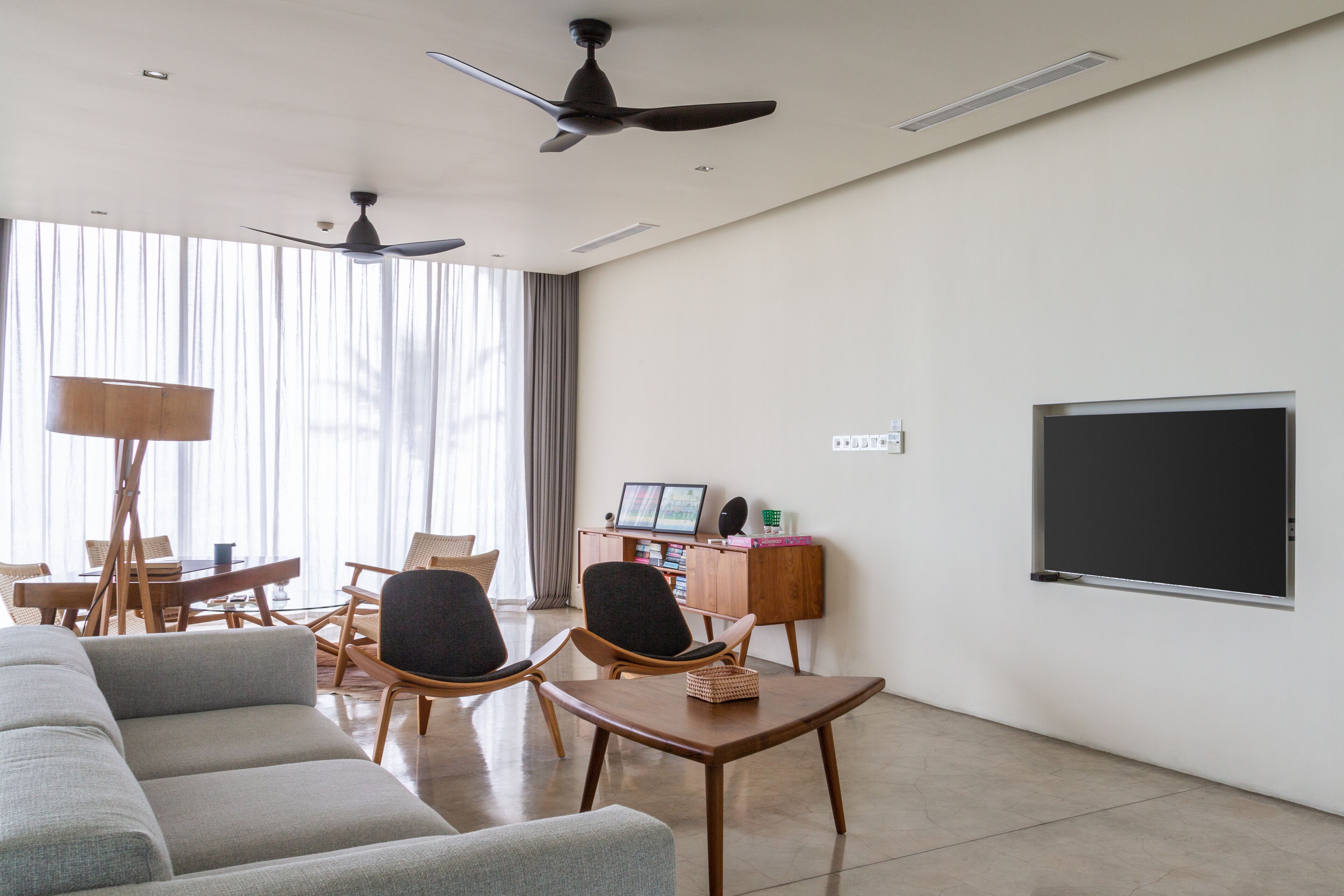 Una sala de estar moderna con sofá, sillones, una mesa de centro, un escritorio con computadora y un amplio ventanal con cortinas.
