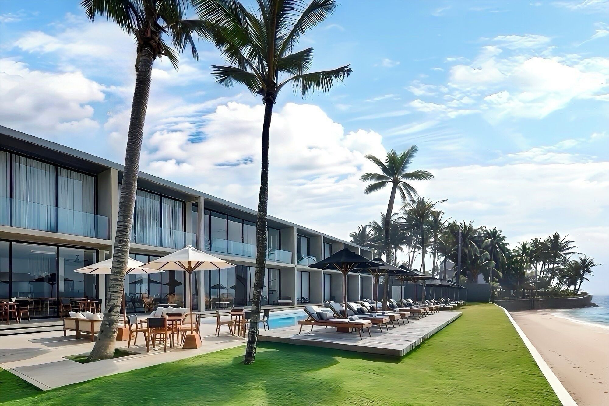 A modern hotel with a poolside area, outdoor seating, and palm trees.
