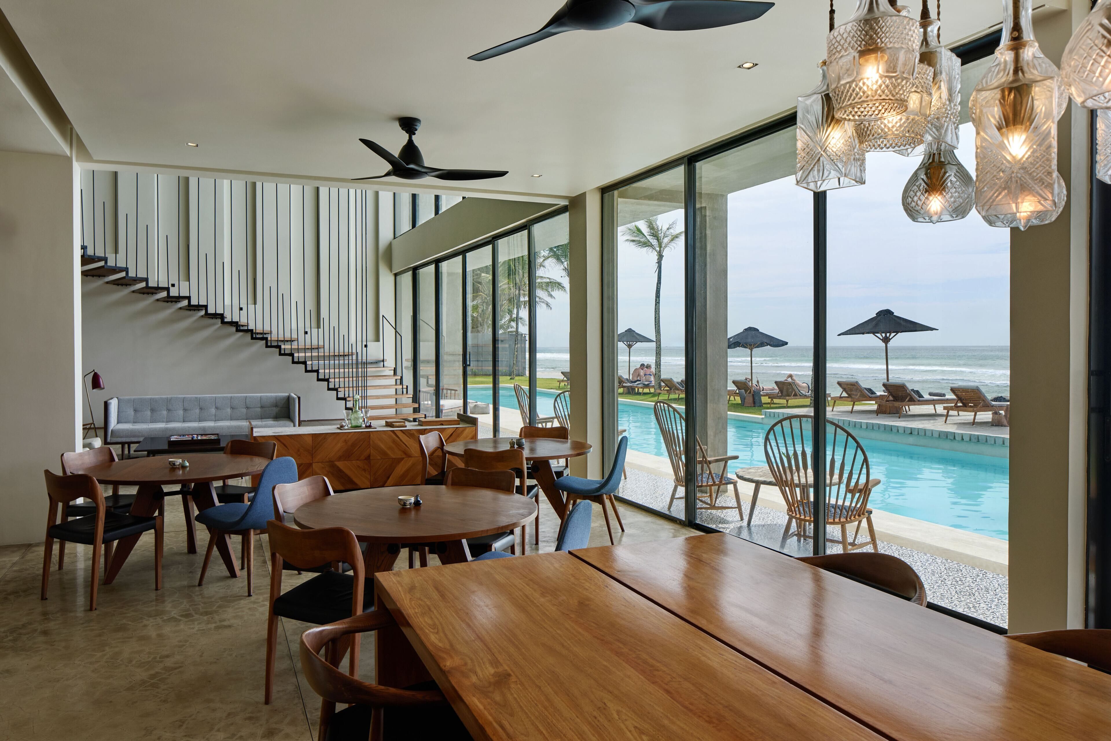 A modern dining area with a pool view, wooden furniture, and a staircase leading to upper floors.